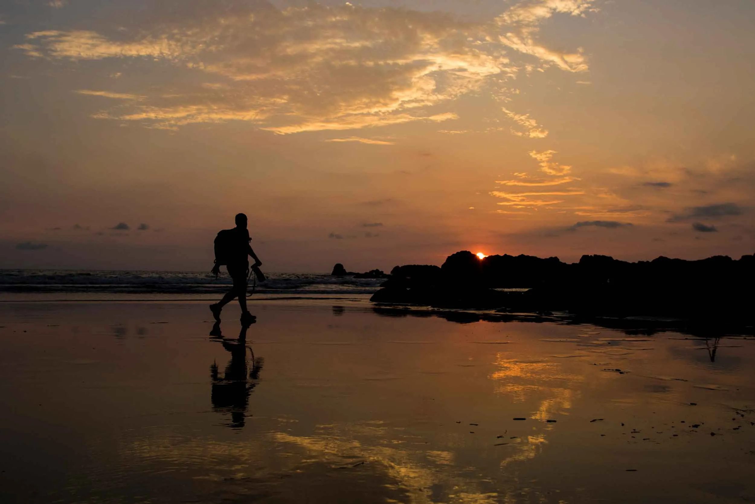 "Beautiful sunset with a photographer walking along the beach shore, holding a camera and capturing the scene."