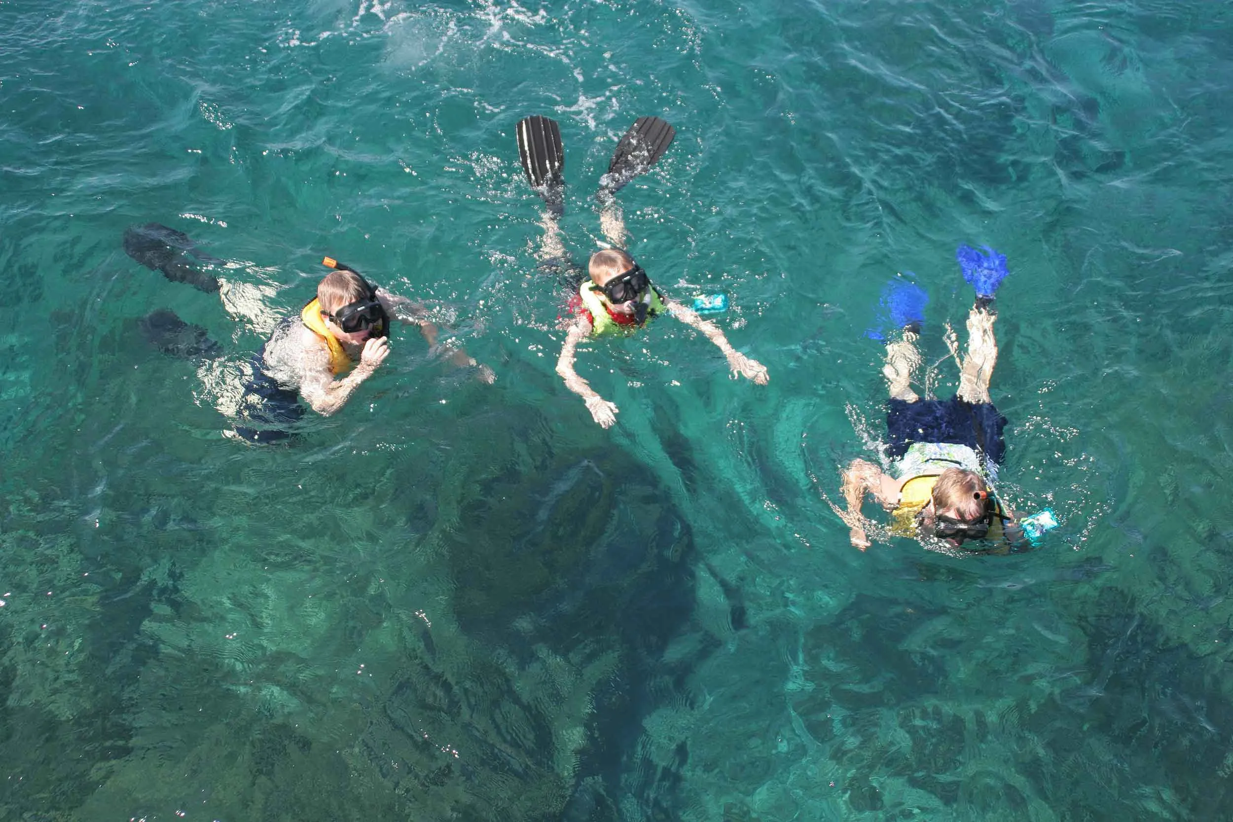 "Three young people snorkeling in clear blue water, exploring underwater marine life with snorkel gear and fins."